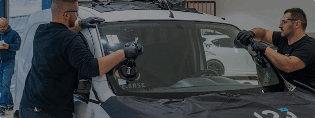 Deux techniciens remplacent un pare-brise.